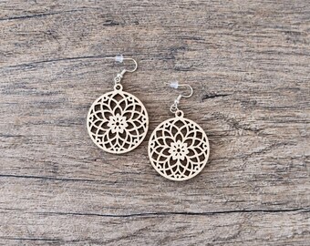 May include: A pair of circular wooden earrings featuring a laser-cut geometric mandala pattern. Each earring is suspended from a silver-toned metal fishhook wire and includes a small, clear plastic backing for secure placement during wear.
