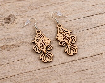 May include: A pair of dangling earrings featuring laser-cut wooden fish pendants. Each pendant displays an intricate, filigree-style cutout pattern within the body and fins of the fish. The earrings are attached to silver-toned metal hooks.