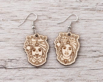 May include: A pair of dangle earrings featuring laser-cut light wood pendants. Each pendant displays a detailed engraved illustration of a royal figure wearing a crown and ornate headwear, suspended from silver-toned metal fishhook ear wires.