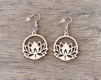 May include: A pair of dangle earrings featuring light-colored wooden charms in a circular frame. Each charm displays a laser-cut lotus flower design with intricate petals and small circular cutouts. The charms hang from silver-toned metal hooks.