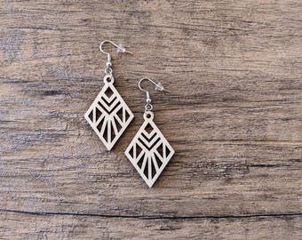 May include: A pair of light-colored wooden earrings featuring a diamond shape with a geometric cutout pattern. The earrings are attached to silver-toned metal hooks with clear plastic backings, showcasing a symmetrical design with clean lines.