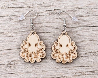 May include: A pair of dangle earrings featuring light-colored wooden octopus charms with laser-engraved details. The octopus designs show a central head with multiple tentacles extending outward. Each charm hangs from a silver-toned metal hook.