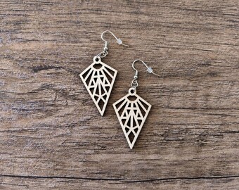 May include: A pair of light-colored wooden earrings featuring a geometric, fan-shaped cutout design. Each earring hangs from a silver-toned metal hook with a small clear plastic backing, showcasing a symmetrical pattern of triangles and lines.