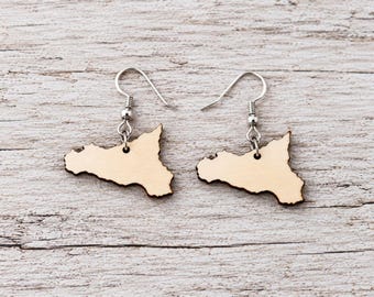 May include: A pair of dangle earrings featuring light-colored wooden pendants shaped like the island of Sicily. Each pendant has a dark, laser-cut edge and is attached to a silver-toned metal fishhook ear wire with a small bead detail.