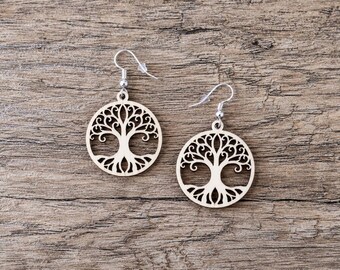 May include: A pair of circular light-colored wooden earrings featuring a laser-cut tree of life design. Each earring is suspended from a silver-toned metal fishhook style ear wire with a small clear plastic backing for secure placement.