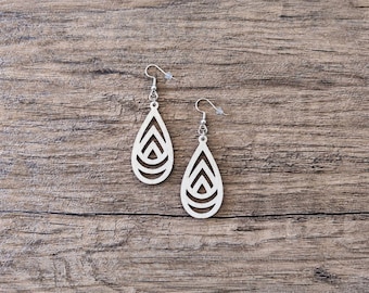 May include: A pair of light-colored wooden teardrop-shaped earrings featuring a cutout geometric pattern of nested triangles and arcs. The earrings are attached to silver-toned metal fishhook ear wires with small clear plastic backings.