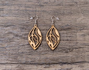 May include: A pair of light brown wooden earrings featuring a laser-cut marquise shape with an intricate, abstract cutout pattern. The earrings are attached to silver-toned metal fishhook wires with clear plastic backings for secure wear.