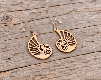 May include: A pair of light brown wooden earrings featuring a laser-cut nautilus shell design. Each earring has a silver-toned metal hook with a clear plastic backing, showcasing a detailed spiral pattern with radiating segments.