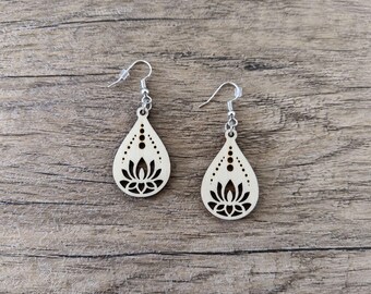 May include: A pair of teardrop-shaped wooden earrings featuring a laser-cut lotus flower design. The light-colored wood has dark brown cutouts of a lotus blossom and small circular accents. Each earring hangs from a silver-toned metal fishhook wire.