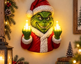 May include: A wall-mounted decorative figure of a green character wearing a red Santa suit with white fur trim and a matching hat. The figure has a mischievous facial expression and holds up both hands with glowing middle fingers illuminated.