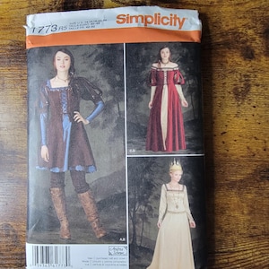 May include: A Simplicity 1773 sewing pattern envelope featuring illustrations of three different costume styles. The package displays a brown tunic with blue sleeves, a red and cream off-the-shoulder gown, and a long cream dress with a crown accessory.