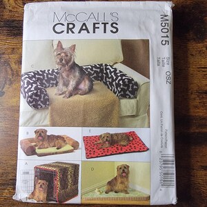 May include: A McCall's Crafts sewing pattern envelope, model M5015, featuring illustrations of various pet beds and crate covers. The front displays images of dogs on different styles of beds, including a bolster bed, a flat mat, and a crate cover.
