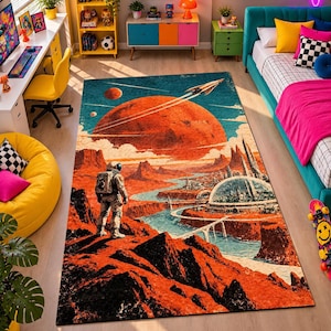 Op de afbeelding: Een rechthoekig vloerkleed met een sciencefictionillustratie van een astronaut op een rotsachtig rood planeetoppervlak, uitkijkend over een futuristische stad met koepels, een kronkelende blauwe rivier en een grote oranje planeet.