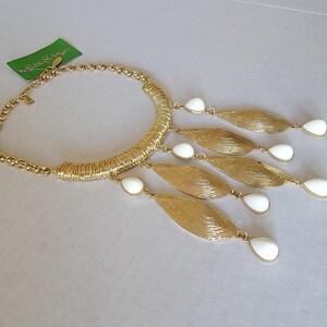 May include: Gold-tone statement necklace with a textured collar and chain. The necklace features five gold leaf-shaped pendants with white teardrop-shaped accents. A green tag is visible.