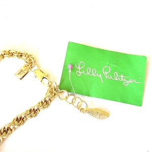 May include: A gold-toned chain necklace with a textured rope design. The necklace is attached to a clasp and an extender chain. A green tag with the words "Lilly Pulitzer" is attached to the necklace.