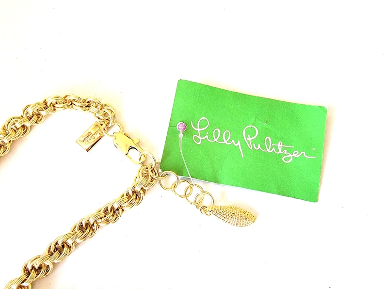 May include: A gold-toned chain necklace with a textured rope design. The necklace is attached to a clasp and an extender chain. A green tag with the words "Lilly Pulitzer" is attached to the necklace.