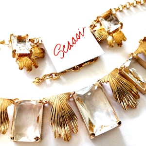 May include: A gold-toned necklace with clear rectangular crystals and fan-shaped accents. The necklace has a delicate chain and a matching bracelet. A tag with the name "Scassi" is visible.