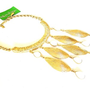 May include: Gold-tone necklace with a chain and a curved, textured centerpiece. The necklace features dangling leaf-shaped pendants with white accents. A green tag with the brand name is attached.