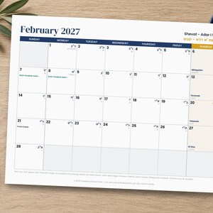 Op de afbeelding: Een wandkalenderpagina voor februari 2027 met een rasterindeling met de dagen van de week in het Engels en Hebreeuws. De koptekst toont February 2027 en Shevat - Adar I 5787. De kalender bevat datums, Hebreeuwse tekst en namen van feestdagen.
