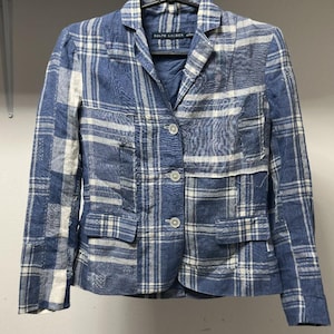 Könnte beinhalten: Ein Ralph Lauren Blazer mit einem blau-weißen Karomuster im Patchwork-Stil. Die Jacke hat ein steigendes Revers, drei Knöpfe auf der Vorderseite, zwei Pattentaschen und lange Ärmel. Der Stoff hat eine strukturierte Optik mit sichtbaren Nähten.