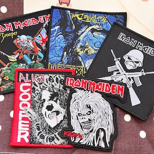 Op de afbeelding: Een verzameling van vijf geborduurde stoffen patches met bandlogo's en grafische illustraties. De patches tonen Iron Maiden- en Alice Cooper-afbeeldingen, waaronder skeletfiguren, een soldaat met een geweer en tekstlogo's in rood, wit en zwart.