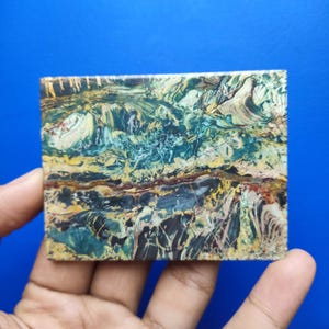 Pode incluir: Uma placa retangular polida de pedra jaspe multicolorida com padrões intrincados em espiral em tons de verde floresta profundo, amarelo mostarda, carvão escuro e castanho terra com inclusões minerais lineares distintas.
