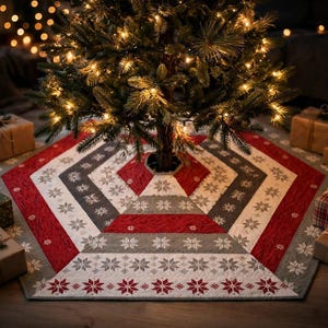 May include: A hexagonal Christmas tree skirt featuring a geometric pattern of alternating red and gray panels. The fabric is decorated with white snowflake motifs and a border of red and white star patterns, placed under a lit Christmas tree.