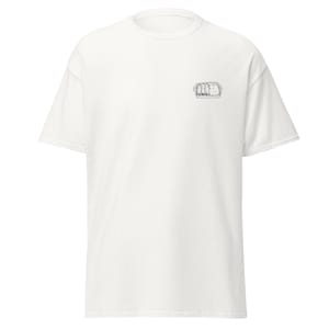 May include: A white short-sleeved t-shirt featuring a small, black-and-white line art illustration on the upper left chest area. The graphic depicts a rectangular baking dish filled with three distinct, textured food portions.