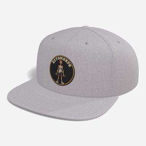 May include: A heather gray snapback cap featuring a circular patch on the front. The patch has a black background with a yellow border and the text ECTOMORPH arched above a cartoon illustration of a thin person holding two dumbbells.