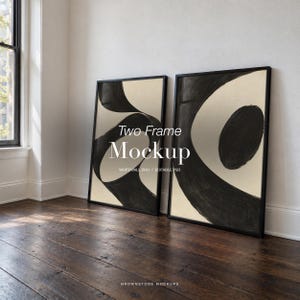 May include: Two rectangular black frames containing abstract art with bold black brushstrokes on a cream background. The text "Two Frame Mockup" and "WHITEWALL DUO / EDITABLE PSD" is centered over the artwork. The frames rest on a dark wood floor.