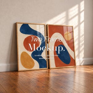May include: Two rectangular wooden frames containing abstract art prints with blue, orange, and yellow organic shapes on a cream background. The text "Two Frame Mockup. 2:3 ARTWORK / EDITABLE PSD BROWNSTONE MOCKUPS" is centered over the artwork.