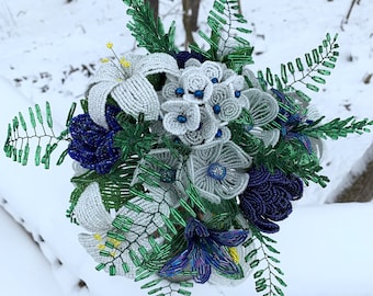 May include: A handcrafted beaded bouquet featuring white, gray, and blue flowers with green accents. The bouquet includes lilies, hydrangeas, and other floral elements, all made with beads. The arrangement is set against a snowy backdrop.