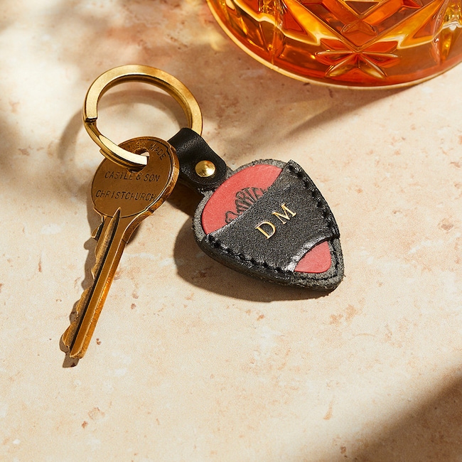 A black leather key chain guitar pick holder shown personalized with gold imprinted initials.