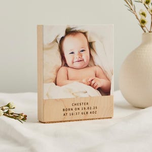 Könnte beinhalten: Ein rechteckiger Holzblock mit einem aufgedruckten Foto eines in eine weiße Decke eingewickelten Babys. Der untere Teil des Holzes zeigt den Text CHESTER, BORN ON 19.02.25, AT 16:37, 6LB 4OZ in einer klaren, schwarzen, serifenlosen Schrift.
