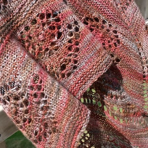 May include: A close-up of a knitted shawl with a delicate lace pattern in shades of brown, pink, and white.