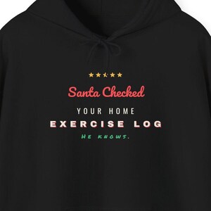 May include: A black hooded sweatshirt featuring a graphic print with five yellow stars above the text "Santa Checked" in red, "YOUR HOME" in white, "EXERCISE LOG" in white with red outlines, and "HE KNOWS." in green at the bottom.