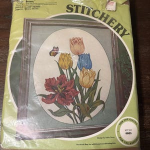 May include: A Paragon Needlecraft stitchery kit titled Tulip Fantasy featuring a printed oval design of red, yellow, and blue tulips with a butterfly. The packaging includes the text Kit No. 0805, Design by Adele Veres, and fits a 22 by 30 inch frame.