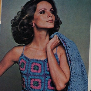 May include: A woman wearing a blue crochet dress with pink and green accents. The dress is made of granny squares and has a sleeveless design.