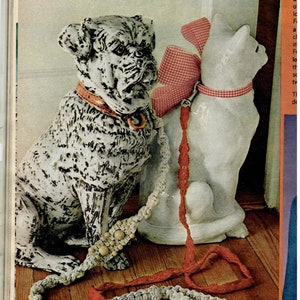 May include: A white ceramic dog and cat figurine with a red and white gingham bow on the cat. The dog and cat are connected by a white and red crocheted leash with wooden beads.