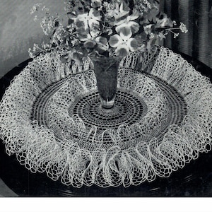 Peut inclure: Un napperon en crochet blanc avec un bord festonné posé sur une table en bois foncé avec un vase de fleurs au centre.