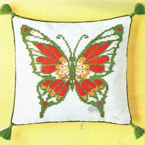 May include: A white pillow with a green border and tassels features a red, yellow, and green embroidered butterfly design.
