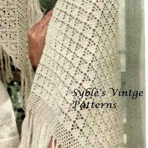 May include: Cream-colored crocheted shawl with fringe, featuring a diamond pattern. The image also shows a straw hat with a pink ribbon and the text "Syble's Vintge Patterns".