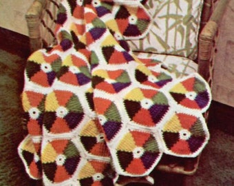 May include: A colorful crocheted blanket with a geometric pattern in shades of red, orange, yellow, green, purple, and black. The blanket is draped over a wicker chair.