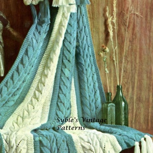 May include: A teal and white knitted throw blanket with a cable knit pattern and tassels. The blanket is draped over a wooden surface with a clock and dried flowers in the background. The text "Syble's Vintage Patterns" is printed on the blanket.