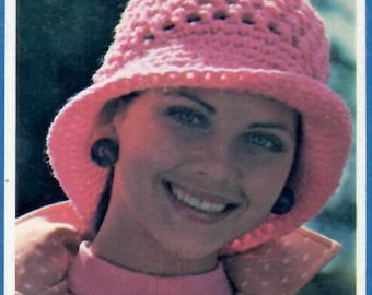 May include: A pink crocheted hat with a wide brim and a delicate openwork design. The hat is worn by a person with brown hair and brown eyes.