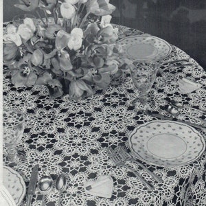 May include: A white crocheted tablecloth with a delicate floral pattern, featuring a bouquet of white and pink tulips in the center. The tablecloth is set with a glass, silverware, and two plates.