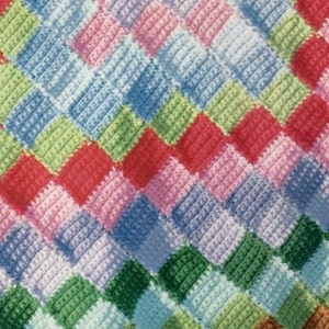 May include: A colourful crocheted blanket with a diamond pattern in shades of pink, blue, green, and red.