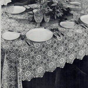 May include: A white crocheted tablecloth with a delicate floral pattern. The tablecloth is laid on a table with plates and silverware set for a formal dinner.