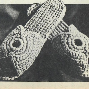 Op de afbeelding: Een paar gebreide pantoffels in de vorm van een vis. De pantoffels zijn wit en hebben een textuur.