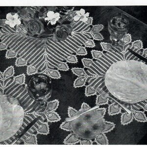 Puede incluir: Una foto en blanco y negro de un camino de mesa y manteles individuales de ganchillo con un diseño de hojas. El camino de mesa y los manteles individuales están colocados sobre una superficie oscura con platos y vasos encima.